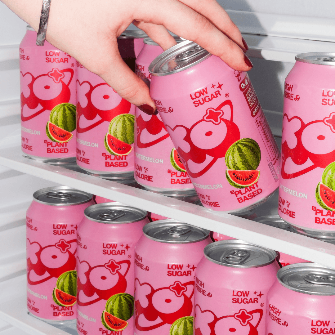 XO Watermelon Soda 12-pack cans in a refrigerator, showcasing low sugar, plant-based drink options.