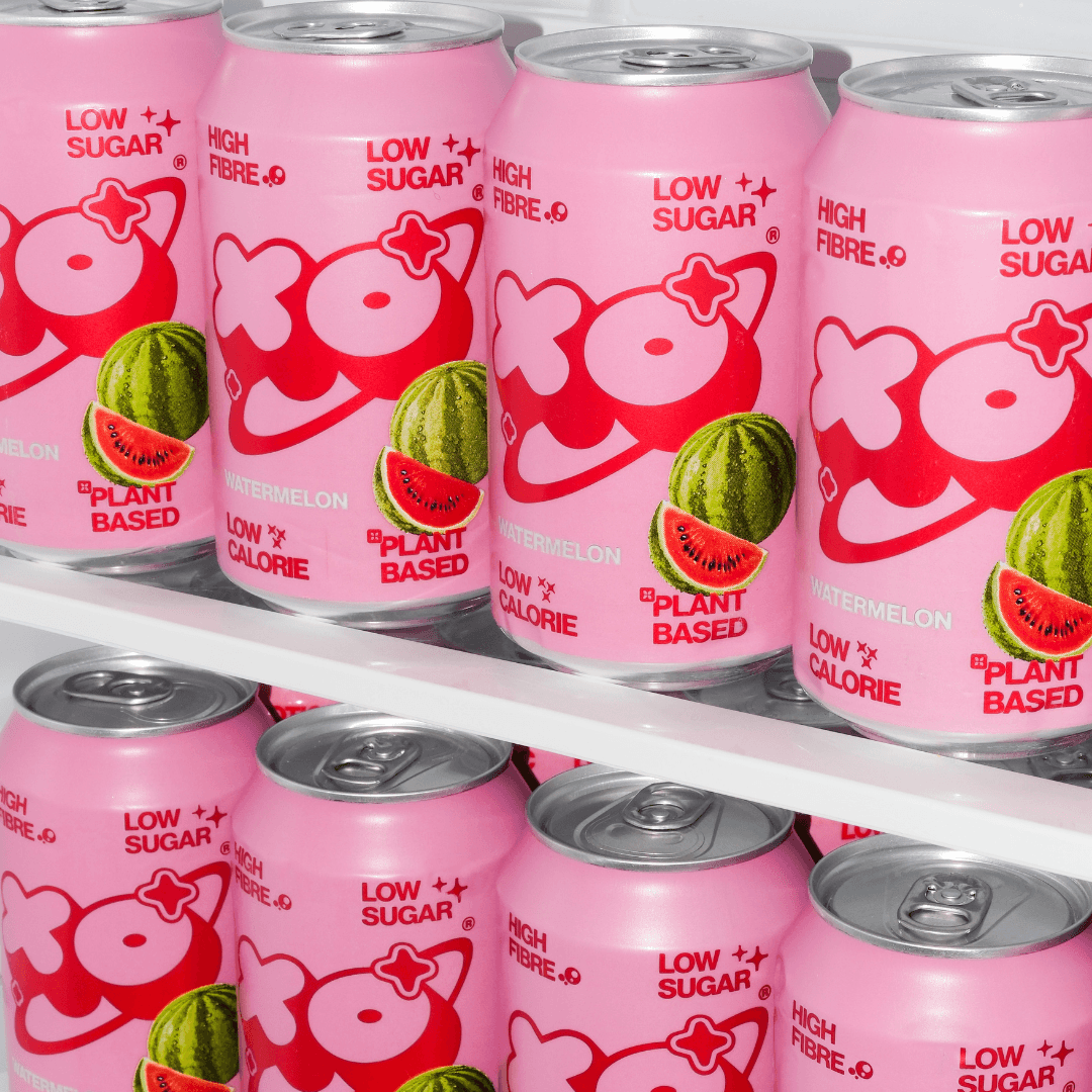 XO Watermelon Soda 12-pack displayed in a fridge, featuring vibrant pink cans with watermelon graphics and health benefits.